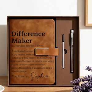 Puede incluir: Un cuaderno de color tostado con cierre magnético y un bolígrafo negro dentro de una caja de regalo marrón. La portada tiene impreso el texto Difference Maker, una definición y el nombre Sophia. Incluye un recambio de tinta adicional.