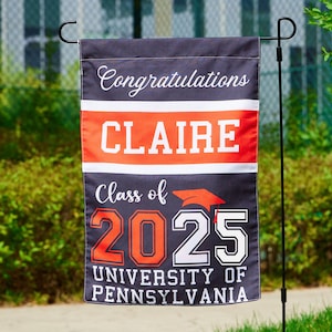 May include: A black and orange graduation yard sign with the text "Congratulations Claire Class of 2025 University of Pennsylvania".