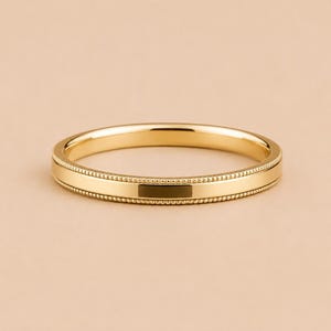 May include: A polished yellow gold band ring featuring a smooth, flat center surface bordered by two delicate, raised beaded edges that run continuously around the entire circumference of the circular metal jewelry piece.