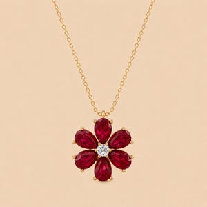 May include: A gold chain necklace featuring a flower-shaped pendant. The pendant consists of six pear-cut deep red rubies arranged as petals around a single, central round-cut clear white diamond, all set in a polished gold metal frame.