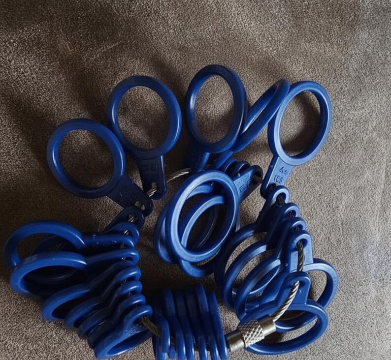 May include: A set of blue ring sizers, connected by a metal cable. The ring sizers are made of plastic and have a loop design. The set includes various sizes for accurate ring measurements. The background is a neutral brown.