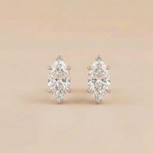 May include: A pair of stud earrings featuring marquise-cut clear stones set in polished silver-toned metal. Each earring has a pointed oval shape with multiple facets that reflect light, secured by a prong setting on a solid metal base.