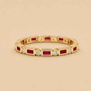 Op de afbeelding: Een gouden ring met een afwisselend patroon van rechthoekige, baguette-geslepen rode robijnen en ronde, briljant-geslepen witte diamanten. De stenen zijn in een doorlopende rij gezet in een gepolijst geelgouden frame, wat een cirkelvormig ontwerp vormt.
