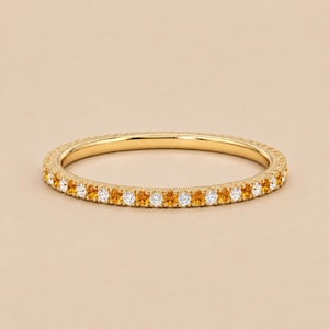 Puede incluir: Un anillo de banda fina de oro con un patrón alterno de piedras preciosas de citrino naranja redondas y facetadas y diamantes blancos brillantes, engastados continuamente alrededor de toda la circunferencia de la banda de oro amarillo pulido.