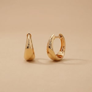 May include: A pair of polished gold hoop earrings with a smooth, rounded surface. One earring is shown from the side, while the other is positioned to display the open hinge mechanism and the circular shape of the hoop design.