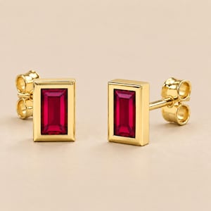 Peut inclure: Une paire de boucles d'oreilles à tige avec des pierres précieuses rouges rectangulaires taille baguette serties dans des montures en or jaune poli. Chaque boucle présente un design géométrique épuré avec des pierres rouges vives.