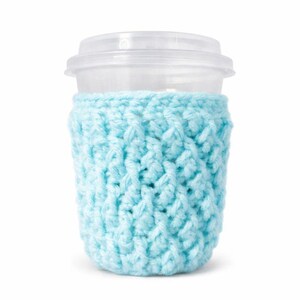 May include: A clear plastic cup with a lid is wrapped in a light blue crocheted cozy. The cozy is made of a textured yarn and fits snugly around the cup, providing insulation and a decorative touch.