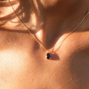 May include: A gold chain necklace with a teardrop-shaped blue gemstone pendant.