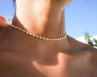 May include: A gold choker necklace with a row of pear-shaped clear stones.