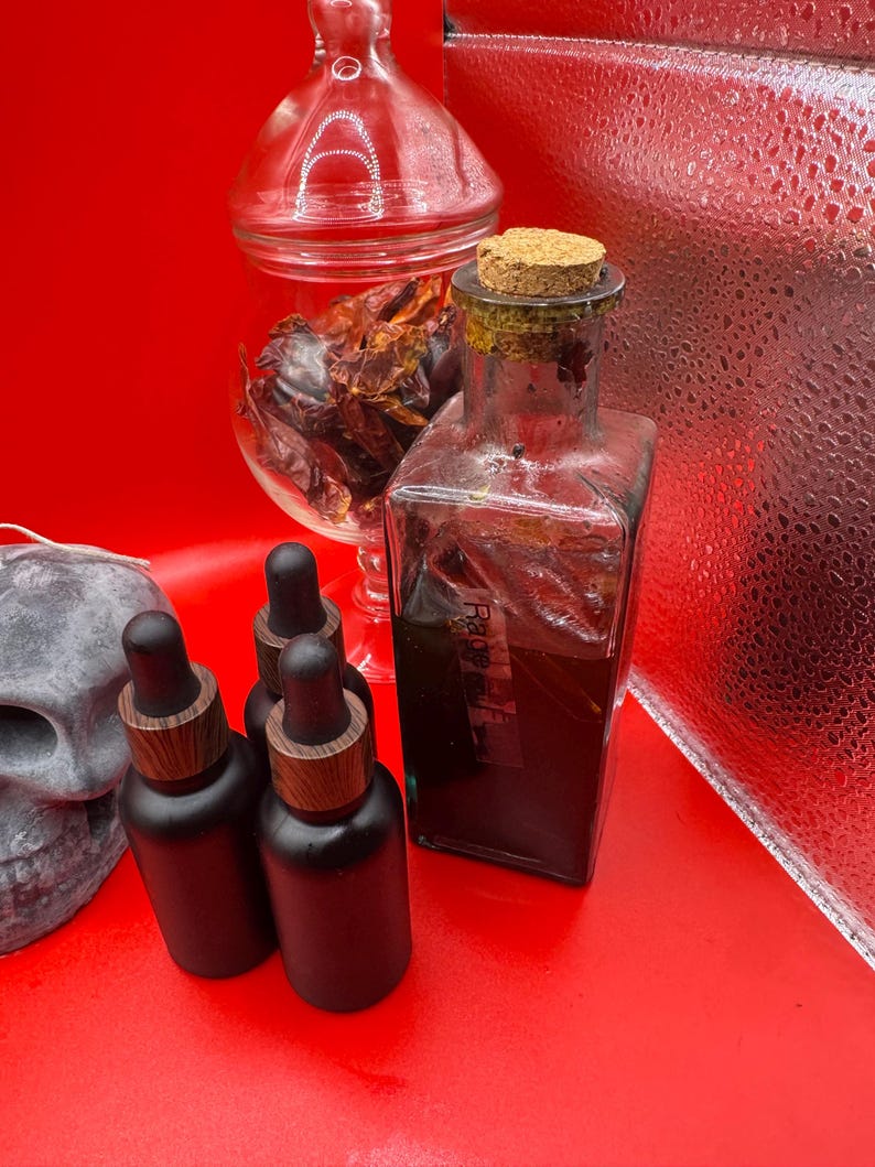 May include: A collection of apothecary-style bottles and jars on a red surface. The image features a clear glass bottle with a cork stopper, several black dropper bottles with wooden tops, and a glass jar filled with dried peppers. A skull is visible on the left.