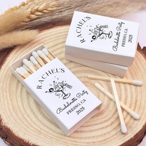 May include: White matchboxes with a black and white illustration of a woman holding a cocktail glass. The matchboxes are labelled "Rachel's Bachelorette Party Fresno, CA 2023".