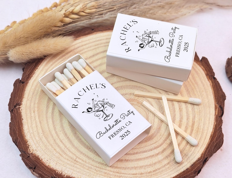 May include: White matchboxes with a black and white illustration of a woman holding a cocktail glass. The matchboxes are labelled "Rachel's Bachelorette Party Fresno, CA 2023".