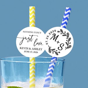 Puede incluir: Un vaso transparente con dos pajitas y pegatinas circulares decorativas. Una pajita es de rayas amarillas y blancas, la otra de rayas azules y blancas. Las pegatinas tienen el texto "Nothing Fancy, just love, Kevin & Ashley, June 17, 2026" y "07.25.2026 M+S".