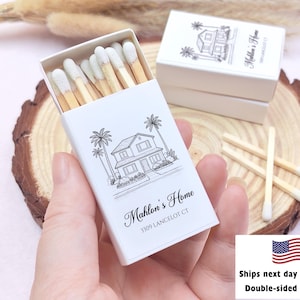 May include: A white matchbox with a black illustration of a house and palm trees. The text "Mahlon's Home" and address are printed on the box. Several matches with white tips are visible inside the open box.
