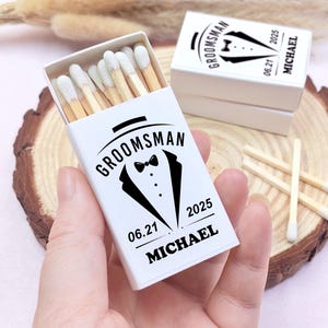 May include: White matchbox with black text and a tuxedo graphic. The text reads "Groomsman 06.21.2025 Michael".