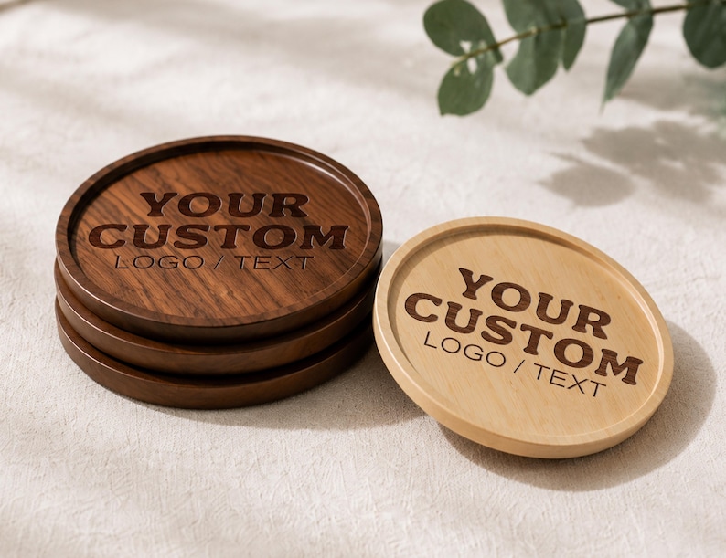 K&ouml;nnte beinhalten: Ein Stapel aus drei dunkelbraunen runden Holzuntersetzern und einem hellbraunen runden Holzuntersetzer. Jeder Untersetzer hat einen erh&ouml;hten Rand und ist mit dem Text YOUR CUSTOM LOGO / TEXT in einer fetten Schrift auf der Fl&auml;che graviert.