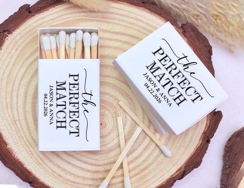 May include: White matchboxes with the text "the PERFECT MATCH" and the names Jason & Anna, along with the date 04.22.2026. The match heads are white, and the wooden matches are displayed on a wooden surface.
