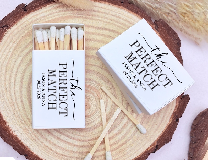 May include: White matchboxes with the text "the PERFECT MATCH" and the names Jason & Anna, along with the date 04.22.2026. The matches have white tips and are displayed on a wooden surface.