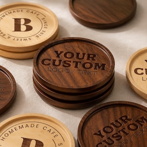 Puede incluir: Una colección de posavasos redondos de madera en tonos claros y oscuros. Algunos posavasos presentan el texto "HOMEMADE CAFE SINCE 2018" con una letra B central, mientras que otros están grabados con "YOUR CUSTOM LOGO / TEXT" en negrita.