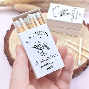 May include: White matchbox with a black and white illustration of a woman in a martini glass. The text on the matchbox reads "Rachel's Bachelorette Party Fresno, CA 2025".