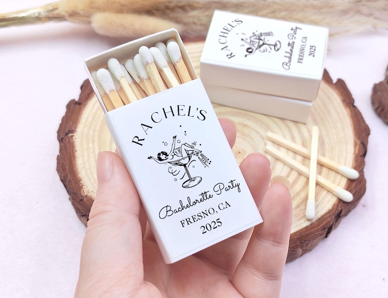 May include: White matchbox with a black and white illustration of a woman in a martini glass. The text on the matchbox reads "Rachel's Bachelorette Party Fresno, CA 2025".