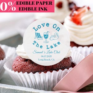 Peut inclure: Gros plan sur des cupcakes au velours rouge avec glaçage blanc et décorations comestibles. Les décorations comestibles indiquent "Love On The Lake" avec des illustrations sur le thème du lac et les détails de l'événement. Le texte "100% Edible Paper Edible Ink" est en haut à gauche.