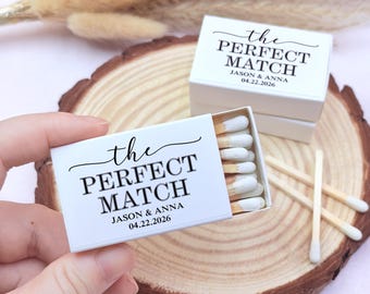 May include: White matchboxes with the text "the PERFECT MATCH" and the names "JASON & ANNA" with the date "04.22.2026" printed in black. The matchbox is open, revealing matches with white tips. The boxes are on a wooden surface.