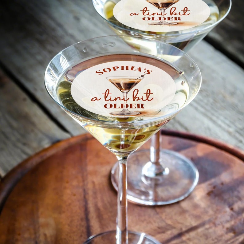 Puede incluir: Dos copas de martini con una pegatina blanca en cada una. La pegatina dice "Sophia's a tiny bit older".