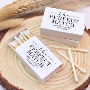 May include: White matchboxes with the text "the PERFECT MATCH" and the names Jason & Anna, along with the date 04.22.2026. The boxes are open, revealing matches with white tips. The boxes are on a wooden surface.