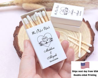 May include: White matchbox with the text "The Perfect Match" and a heart-shaped design with two swans. The box is personalized with names and a date. Matches are visible inside the box.