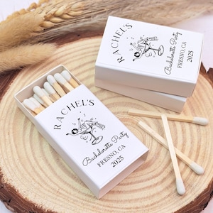 May include: White matchboxes with a black and white illustration of a woman holding a cocktail glass. The matchboxes are labelled "Rachel's Bachelorette Party Fresno, CA 2023".