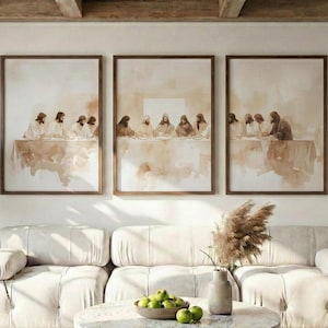 Op de afbeelding: Drie ingelijste kunstprints met een religieuze scène hangen boven een crèmekleurige bank. De prints hebben een sepia-kleurige aquarel, met een tafelsetting en figuren. Een ronde salontafel en een potplant maken de kamer compleet.