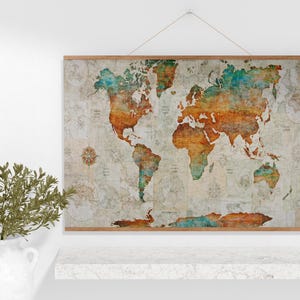 May include: World map art print with a vintage, distressed look. The map features a color palette of orange, teal, and cream, mounted on a wooden frame. The print is hanging on a white wall, with a decorative plant in a white vase.