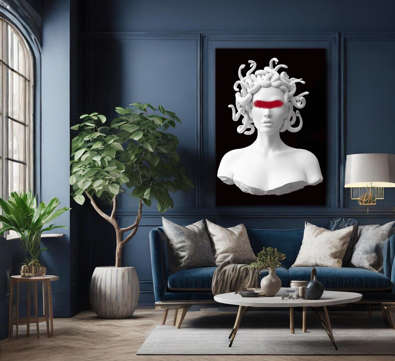 May include: A white Medusa bust with a red stripe across the eyes is displayed on a black background. The artwork is mounted on a dark blue wall above a blue sofa with decorative cushions. A potted plant and a side table are in the foreground.