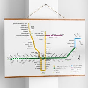 Op de afbeelding: Een ingelijste metrokaart met een houten frame, met gekleurde lijnen die verschillende routes vertegenwoordigen. De kaart toont stationsnamen en routedetails, met een sleutel onderaan. De kaart hangt aan een witte muur.