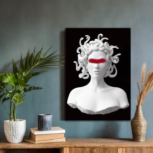 May include: A white sculpture of Medusa with a red band across the eyes, set against a black backdrop. The artwork is displayed on a wall, with a wooden table and decorative items in the foreground.