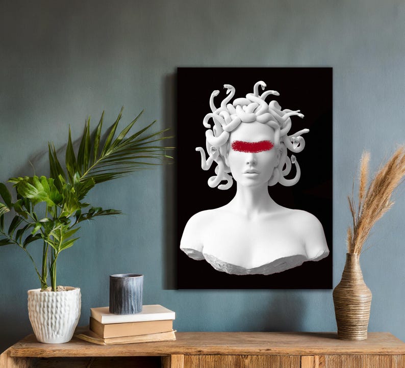 May include: A white sculpture of Medusa with a red band across the eyes, set against a black backdrop. The artwork is displayed on a wall, with a wooden table and decorative items in the foreground.