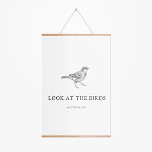 May include: A white poster with a wooden frame and a hanging string. The poster features a detailed black and white illustration of a bird and the text "LOOK AT THE BIRDS" and "MATTHEW 6:26".