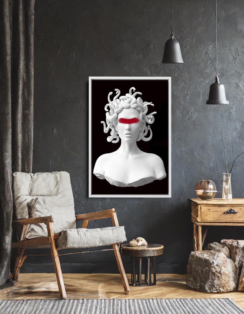 May include: A framed art print depicting a white bust of Medusa with a red band across the eyes, set against a black backdrop. The artwork is displayed in a room with a wooden chair, side table, and dark walls.