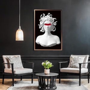 May include: A framed art print depicting a white bust of Medusa with a red band across the eyes, set against a black backdrop. The artwork is displayed in a room with two armchairs, a coffee table, and a hanging light.