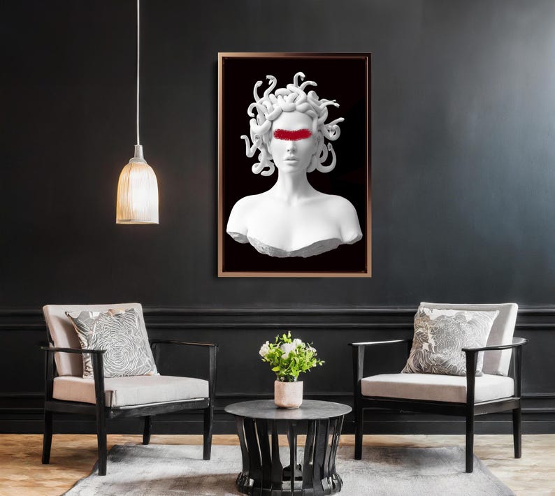 May include: A framed art print depicting a white bust of Medusa with a red band across the eyes, set against a black backdrop. The artwork is displayed in a room with two armchairs, a coffee table, and a hanging light.