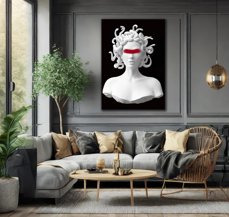 May include: A white bust of Medusa with a red stripe across the eyes, set against a black background. The artwork is displayed in a modern living room with a grey sofa, gold cushions, and a wooden coffee table.