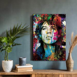 Puede incluir: Un retrato vibrante de una persona con salpicaduras de pintura coloridas y acentos de estilo graffiti. La obra presenta un rostro con una expresión neutra, con trazos audaces de azul, rosa, amarillo y verde. El estilo es una mezcla de arte pop y arte callejero.