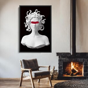 May include: A framed art print depicting a white bust of Medusa with a red band across the eyes, set against a black backdrop. The artwork is displayed in a room with a fireplace, a wooden chair, and a circular rug.