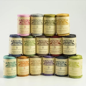 May include: A collection of 14 spools of natural twine, each with a different colour and labelled with the brand name "Nutscene" and a descriptive name like "Pinktwist" or "Blacktwist". The twine is described as "The Ideal Garden Twine" and is soft, pliable, and strong.