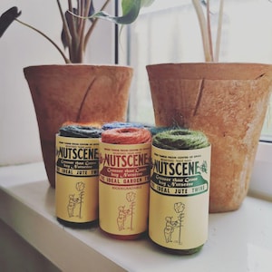 May include: Three rolls of natural jute twine, each with a different coloured label. The labels are yellow with green text and feature the brand name "Nutscene" and the text "Greener than Green buy Nutscene The Ideal Jute Twine". One label also includes the text "Biodegradable".