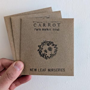 May include: A stack of brown paper seed packets with black text and a floral illustration. The text reads "CARROT Paris Market Atlas NEW LEAF NURSERIES".