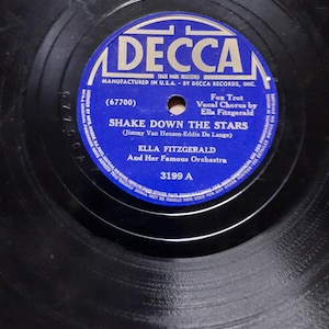 Könnte beinhalten: Eine Vintage-Vinyl-Schallplatte mit einem blau-weißen Etikett mit dem Text "DECCA" und dem Songtitel "SHAKE DOWN THE STARS" von Ella Fitzgerald. Die Schallplatte ist schwarz mit sichtbaren Rillen und das Etikett enthält den Text "Fox Trot" und "3199 A".