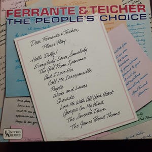 Peut inclure: Un album vinyle vintage de Ferrante & Teicher, intitulé "The People's Choice". La pochette présente le titre en rouge et bleu, avec une note manuscrite listant des titres de chansons comme "Hello Dolly!" et "The James Bond Theme."