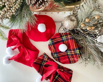 May include: A set of three red and white Christmas hats. Two of the hats are trimmed with white pom-poms and a red ribbon. The third hat has a plaid pattern with red, yellow, and black.